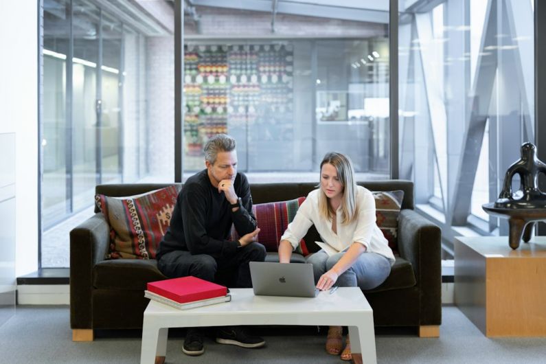 Real Estate Agent - man and woman sitting on couch using macbook