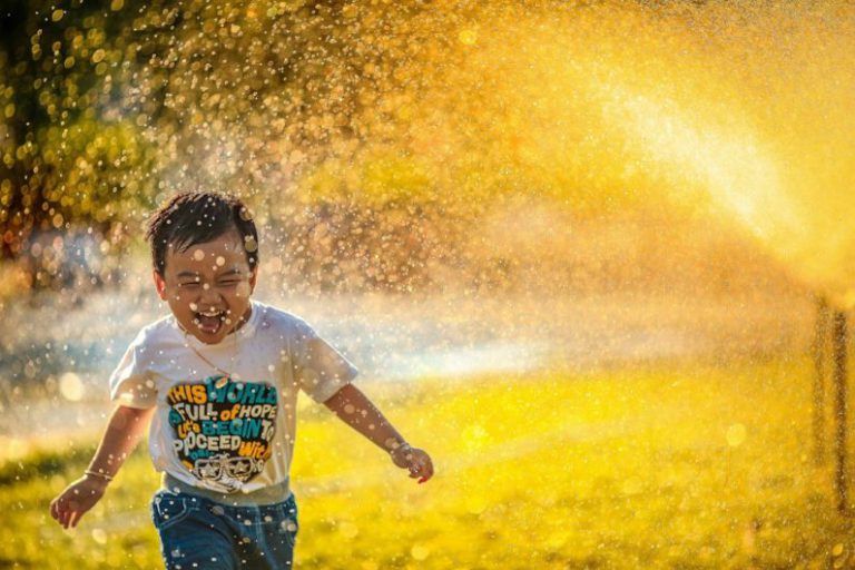 Kid-friendly Backyard - a young boy running through a sprinkle of water